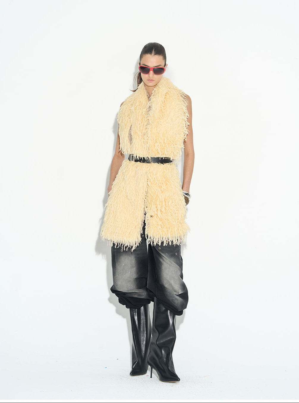 Person wearing a beige fringed scarf, black leather pants, and black high-heeled boots on a white background